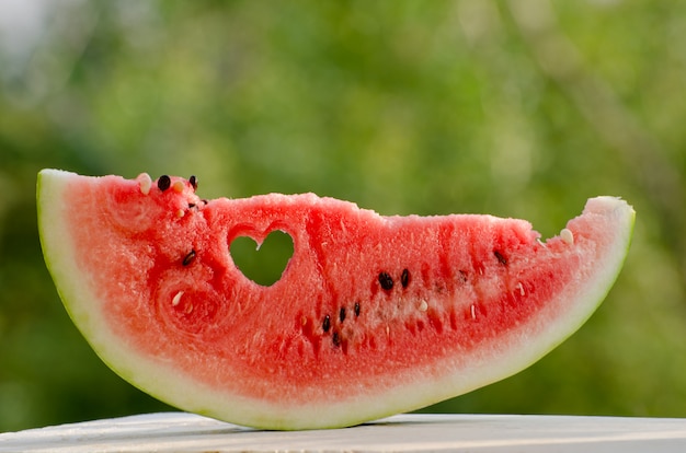 Groot stuk watermeloen met een hart gesneden in het vlees tegen de achtergrond van groen