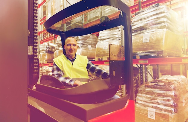 groothandel, logistiek, lading, verzending en mensenconcept - glimlachende man of lader die heftrucklader in het magazijn bedient