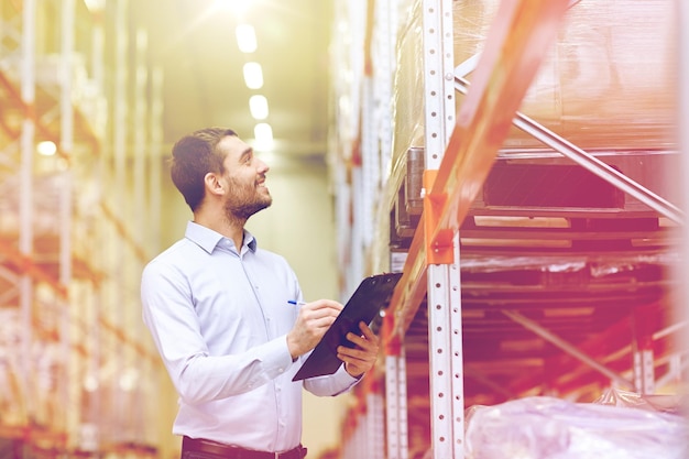 groothandel, logistiek, zaken, export en mensenconcept - gelukkige man of manager met klembord die goederen in het magazijn controleert