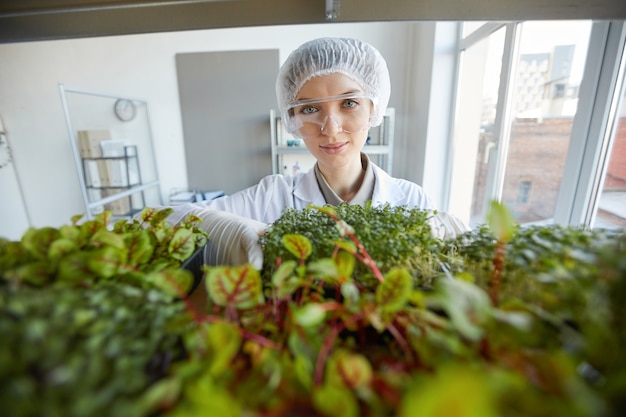 Groothoek portret van glimlachende vrouwelijke wetenschapper plant monsters te onderzoeken tijdens het werken in biotechnologie lab, kopieer ruimte