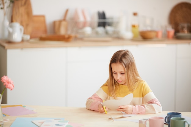 Groothoek portret van schattig meisje kerstkaart maken voor moederdag of valentijnsdag zittend aan tafel in gezellig interieur, kopie ruimte