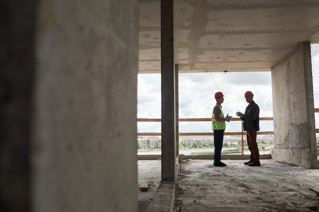 Groothoekbeeld bij twee arbeiders die engineering bespreken op de kopieerruimte van de bouwplaats