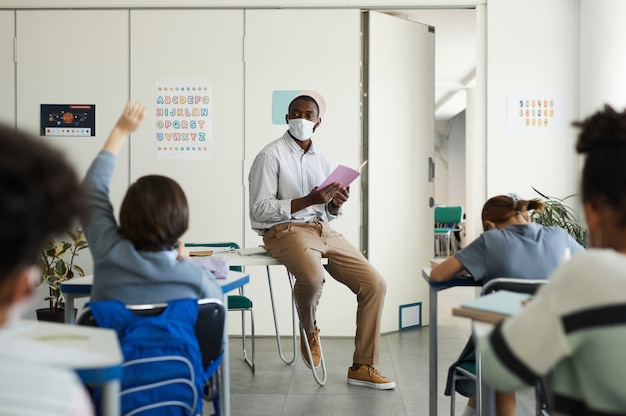 Groothoekportret van Afro-Amerikaanse leraar met masker in schoolklas, covid-veiligheidsmaatregelen, kopieerruimte