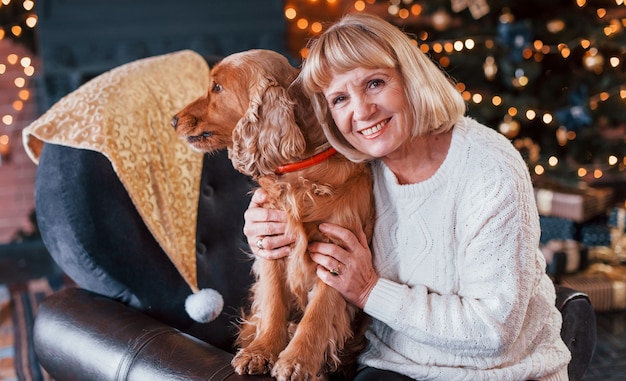 Grootmoeder binnenshuis met hond in kerst ingerichte kamer.