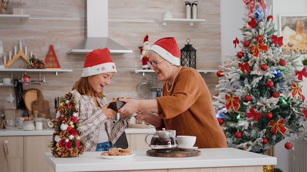 Grootmoeder brengt een wikkelcadeau met lint erop naar kleindochter die geniet van de kerst