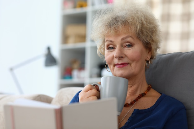 Grootmoeder drinkt koffie en leest een boek in appartement