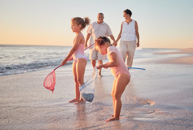 Grootouders en kinderen op het strand met visnetten en plezier maken Jonge kinderen en senior koppel genieten van vakantie met kleinkinderen en pensioen samen Spelen aan zee in de zomer met familie