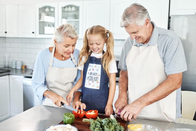 Grootouders meisjeskind in de keuken en koken van gezond voedsel met groenten op snijplank voor gelukkige familielunch thuis Natuurlijke biologische voeding en schoon dieet voor senioren met pensioen