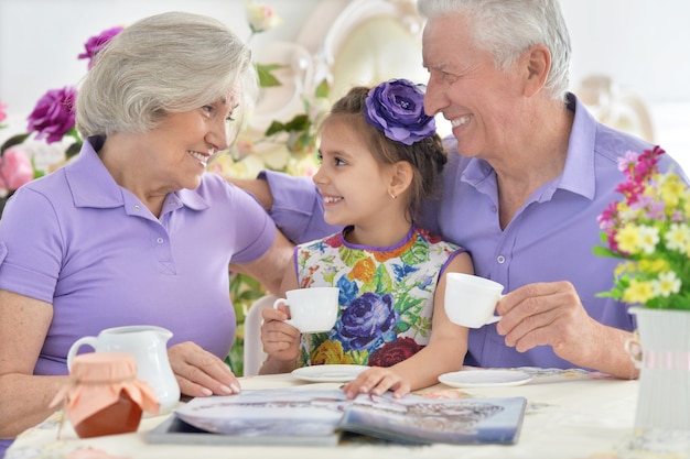 Grootouders met kleindochter die thee drinken en tijdschrift lezen