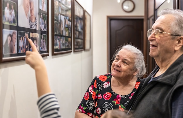 Grootouders tonen de familiefoto's van hun kleindochters aan de muur in huis.