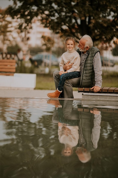 Grootvader brengt op herfstdag tijd door met zijn kleindochter bij een klein waterzwembad in het park