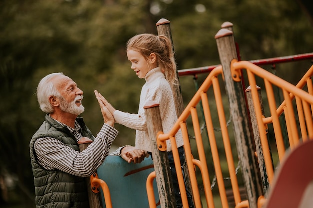 Grootvader brengt op herfstdag tijd door met zijn kleindochter in de speeltuin van het park