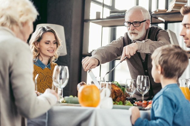 Foto grootvader die kalkoen snijdt voor familie op thanksgiving-vakantiediner