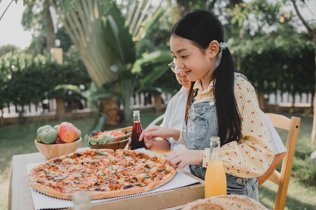 Grootvader en kleindochter hebben pizza in de tuin thuis. Pensioenleeftijd levensstijl met familie op zomervakantie.