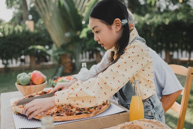 Grootvader en kleindochter hebben pizza in de tuin thuis. Pensioenleeftijd levensstijl met familie op zomervakantie.