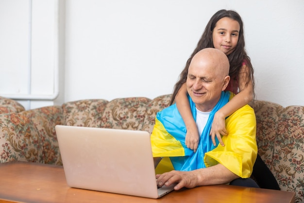 Grootvader en kleindochter met laptop en vlag van Oekraïne
