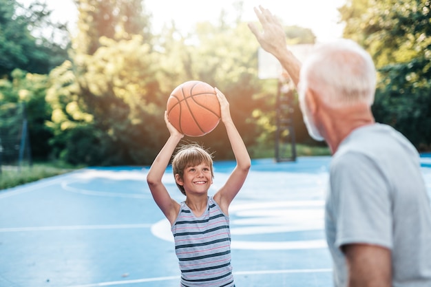 Grootvader en zijn kleinzoon genieten op een mooie zonnige dag en spelen basketbal.