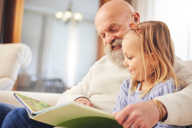 Grootvader kind en familie lezen op een bank in de woonkamer met liefde en leerondersteuning Gelukkig huis en kind met een oudere man in een huis met een verhalenboek en jeugdonderwijs op een bank