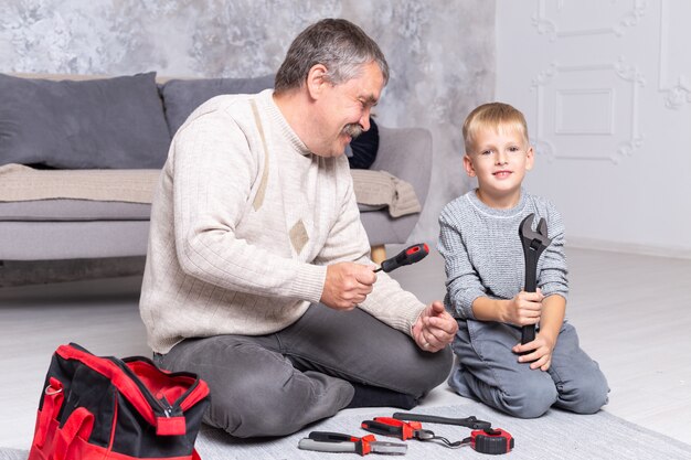 Grootvader laat zijn kleinzoon reparatiegereedschap zien terwijl hij op de grond bij de bank zit