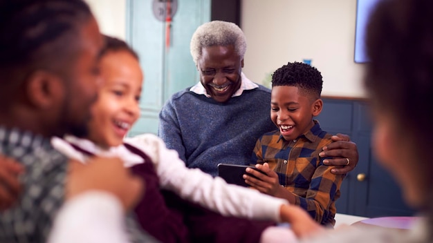Grootvader met kleinkinderen die thuis een spel spelen op mobiele telefoon