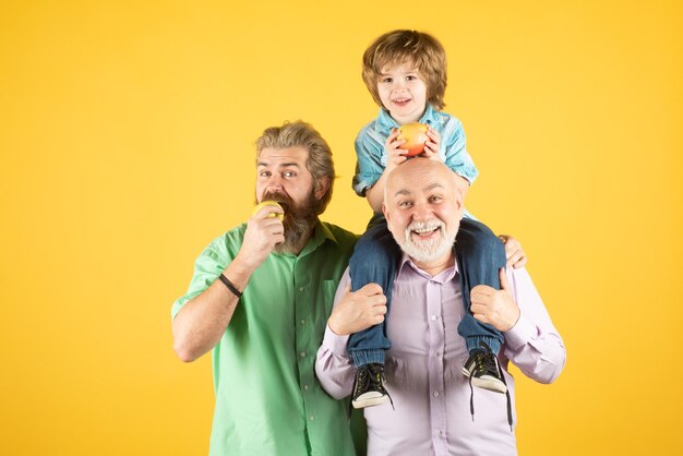 Grootvader vader en kleinzoon knuffelen en eten appelmannen in verschillende leeftijden geïsoleerd op geel