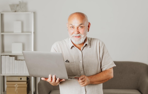 Grootvaderportret van senior man met een laptop Senior man met een grijze baard thuis Volwassen man met computer