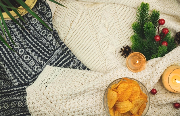 Рифленые чипсы попато в прозрачной миске на уютном фоне, свитер, зимнее украшение, композиция с копией пространства. Фото высокого качества