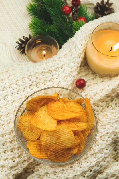 Grooved popato chips in transparent bowl on cozy background, sweater, winter decoration, composition with copy space. High quality photo