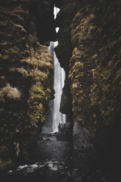 Foto grot van een waterval in ijsland met muren bedekt met mos en twee mensen op de achtergrond bij het water