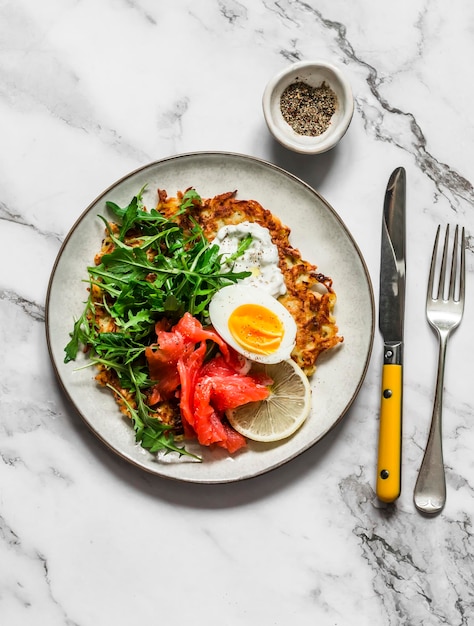 Grote aardappel rosti met ei rucola zalm en Griekse yoghurtsaus op een lichte achtergrond bovenaanzicht Heerlijk eten