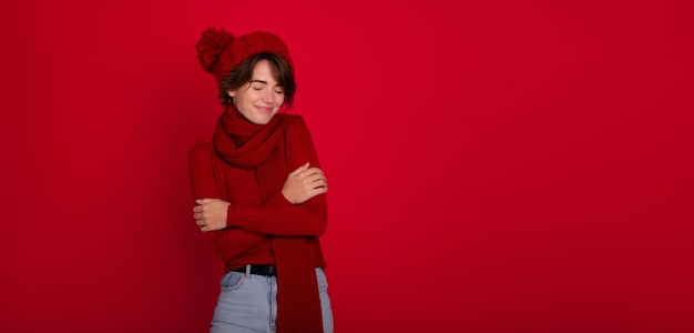 Grote banner foto van vrolijke jonge vrouw presenteren seizoensgebonden winter promotionele aanbieding op rode kopie ruimte Leuke brunette dame in rode winter sjaal trui en hoed Nieuwjaar en Kerstmis