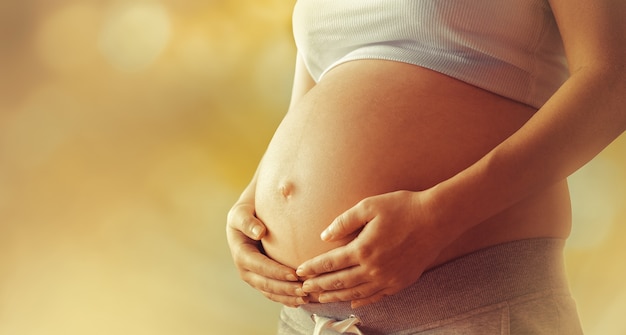 Grote buik van een zwangere vrouw tegen gele bokehachtergrond