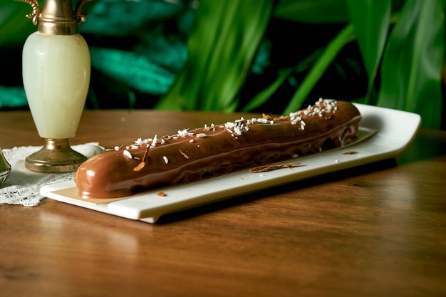 Grote chocolade-eclair met kokos en chocoladeschilfers op houtachtergrond