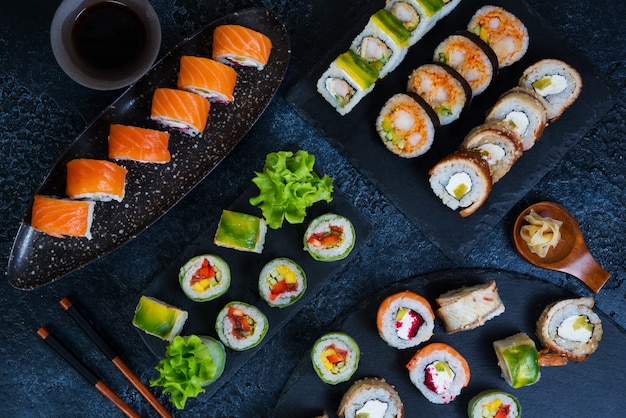 Grote diverse reeks sushi rolt op een zwarte houtskooltribune op een zwarte achtergrond. Traditioneel Japans eten. Bovenaanzicht.