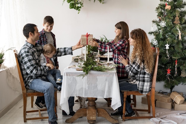 Grote familie heeft een kerstontbijt aan tafel in de woonkamer vader geeft een doos met een cadeau aan een dochtertje voor het nieuwe jaar Feestelijke tafel voor kinderen en ouders Vrolijk kerstconcept