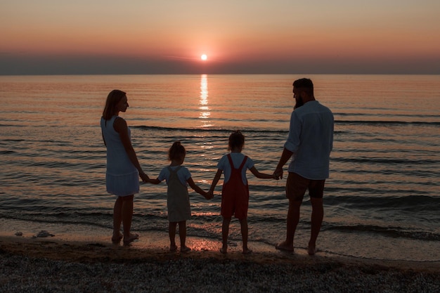 Grote familie op het strand. silhouetten van mensen tegen de zonsondergang. 4 mensen hand in hand