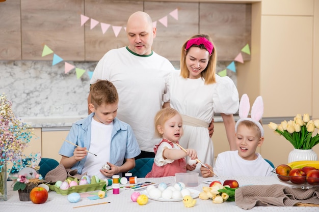 Foto grote gelukkige familie die zich voorbereidt op pasen schattige kinderen die eieren schilderen thuisactiviteit concept van eenheid en liefde broer en zus