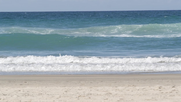 Grote golven van de Stille Oceaan spatten, Californië kust VS. De textuur van het wateroppervlak en zeeschuim. Zeegezicht dichtbij zandstrand, blauw water. Lage hoekmening van turquoise tij. Zonnige tropische winderige zomerdag.