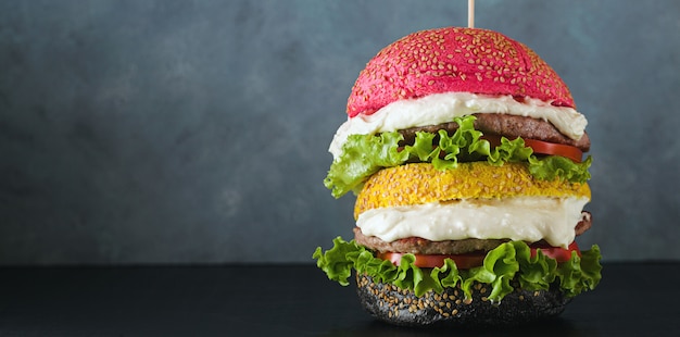 Grote hamburgers met verschillende kleuren broodjes in rood, geel en zwart met parmezaanse room en tomaten, salade op tafel.