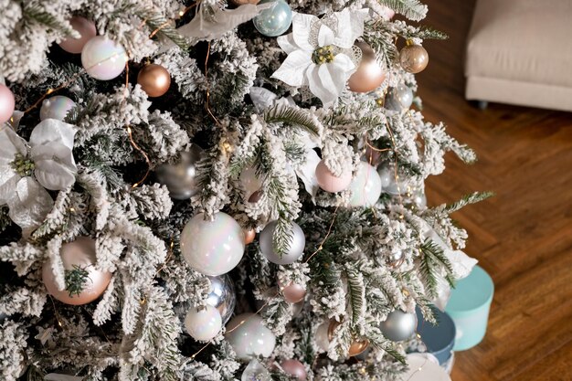 grote kerstboom in een helder interieur met zilveren roze bronzen ballen en sneeuw op de takken Present dozen onder de boomHet concept van Nieuwjaar en Kerstmis Luxe kerstboom met gloeiende krans