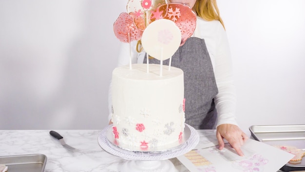 Grote lolly's met sneeuwvlokken in de hoge witte ronde taart steken als laatste versiering.