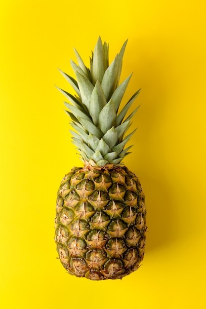 Grote rijpe fruitananas op een felgele tafel. zomer. bovenaanzicht.