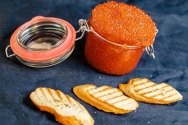 grote rode kaviaar in een pot, oppakken met een lepel, ligt op perkament, naast een stokbrood