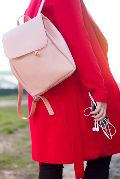 Grote roze rugzak en telefoon met koptelefoon in de arm van het meisje in een modieuze rode jas