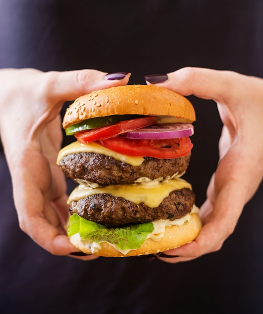 Grote sandwich - hamburgerburger met rundvlees, kaas, tomaat en tartaarsaus in vrouwelijke handen