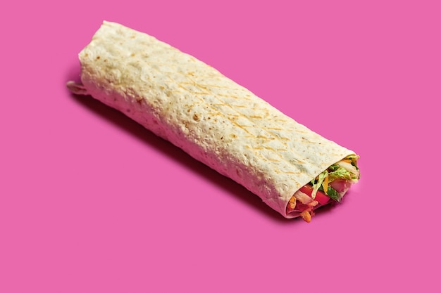 Grote shoarma met kip, groenten en saus op een roze achtergrond.