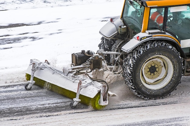 Foto grote sneeuwploegende tractormachine aan het werk op de weg tijdens een sneeuwstorm in de winter.