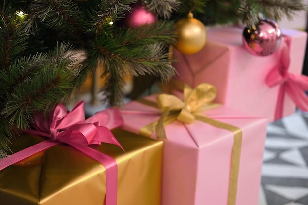 Foto grote verpakt cadeau dozen is onder de kerstboom roze en gouden cadeau verpakt doos met lint voor vrienden familieleden close up verpakking van xmas geschenken feestelijke decoraties voorbereiding voor de feestdagen