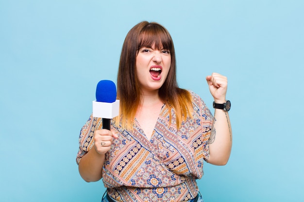 Grote vrouw die agressief schreeuwt met een boze uitdrukking of met gebalde vuisten om succes te vieren