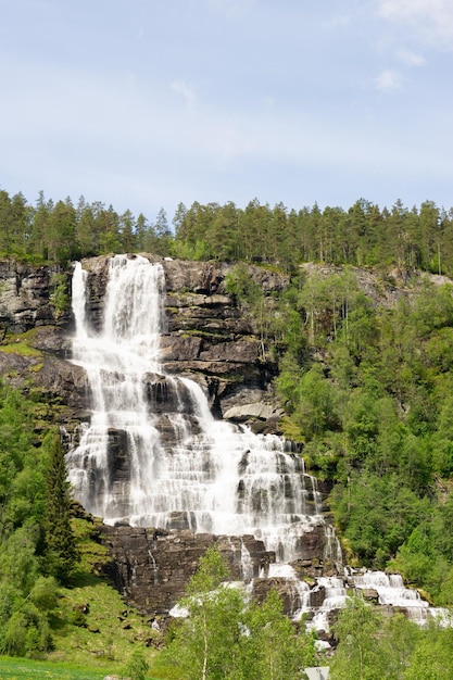 Grote waterval die oprijst in de bergen, omringd door groene bomen in Noorwegen